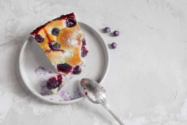 A slice of homemade clafoutis cherry pie - traditional french dessert in a gray plate A slice of homemade clafoutis cherry pie - traditional french tart in a in a gray plate with a spoon on a gray background top view clafoutis stock pictures, royalty-free photos & images