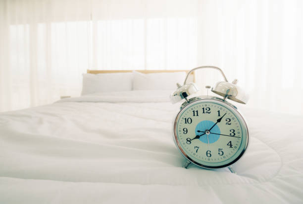 istock Alarm clock on bed in bedroom at morning with sun light. 1261661674