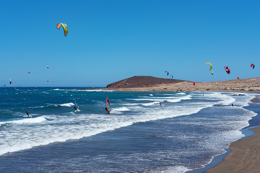 El Medano, Granadilla de Abona, Tenerife, Canary Islands, Spain - June 20, 2020: Montana Roja beach side with surfers enjoying a windy day practicing water sports such as kite surfing or kite boarding.