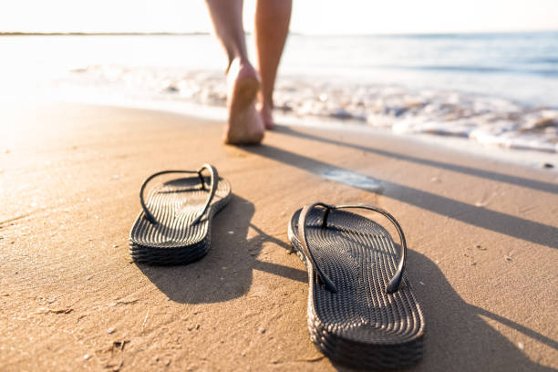 las piernas de mujer se alejan de sus sandalias hacia el agua del mar en una playa - one person beautiful barefoot beach fotografías e imágenes de stock