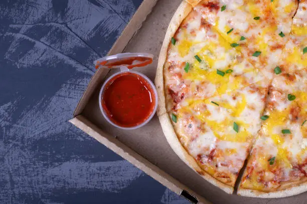 Photo of Pizza with cheese in the cardboard box on the grey table