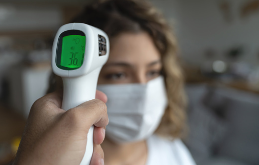 Woman at home checking her temperature with an infrared thermometer - COVID-19 pandemic concepts