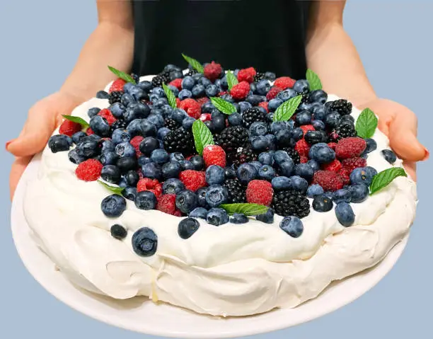 Photo of Pavlova's meringue dessert with blueberries, blackberries, raspberries on a large white plate in the hands of a girl