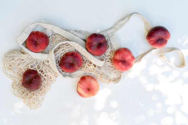 istock Ripe peaches in a string bag on a white wooden background. Flat lay. 1261699296