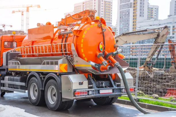 Photo of Pumping water from sewage canals during the construction of roads in the city. Truck with orange water tank.