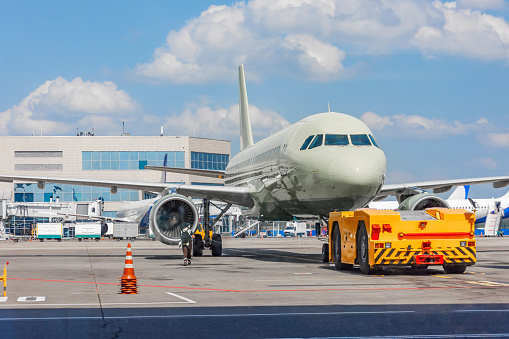 Towing a passenger plane using special equipment for aircraft maintenance. Departure flight in the background of the terminal building