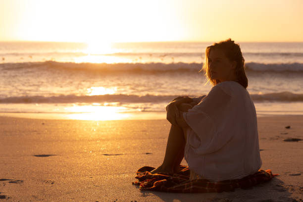 istock Beautiful woman sitting on the beach during sunset 1261730431