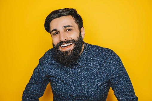 Studio portrait of smiling Indian young hipster bearded male over yellow background.