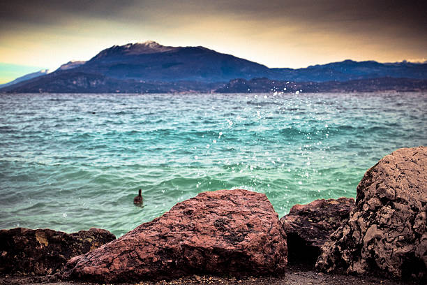 Storm at Garda Lake, Italy. Focus on the rocks in the foreground. Grainy.