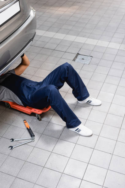 istock mechanic in uniform lying under car near metallic tools 1261798593