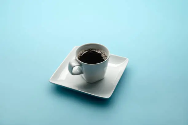 This is a photograph taken in the studio of a modern Coffee cup with black coffee on a baby blue powder background