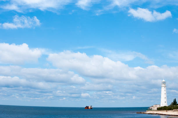 Lighthouse and sunken ship. Sunshine summer day.
