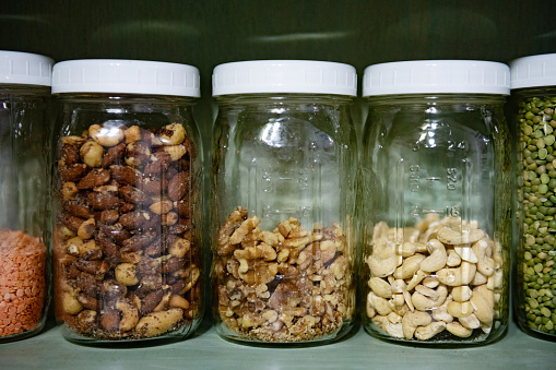 This is a candid photograph of a kitchen pantry shelf lined with jars full of vegan dry food including almonds, walnuts and cashew nuts at home.