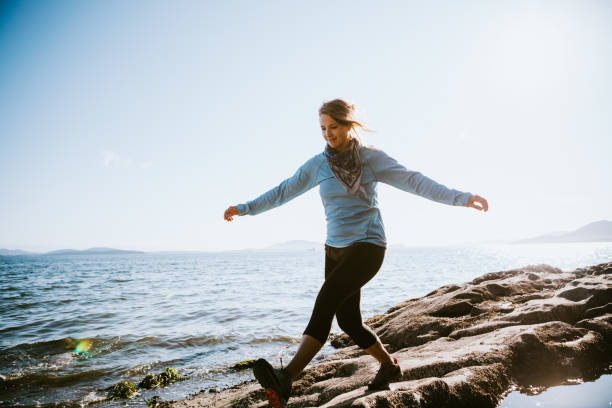 A millennial aged woman enjoys a beautiful walk on a Pacific Northwest beach on the Puget Sound.   She balances on rocks and explores tide pools.