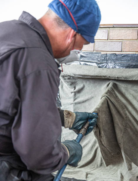 istock Chimney sweep cleaning a traditional fireplace with face covering and protective clothes. 1261877149