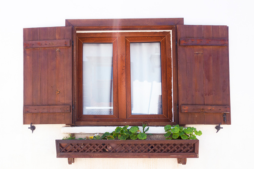 Old window in wooden frame and with closed shutters, with green plants around and an old brick wall. Part of the interior of an outdoor cafe. Torun, Poland, August 2023