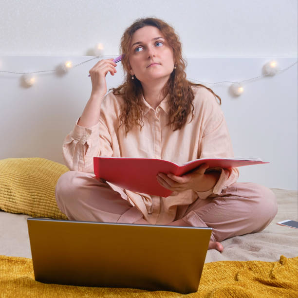 istock Sad girl sitting with laptop on bed. Problems with online education from home 1262026356