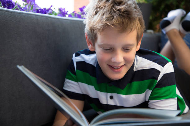 istock Young 10y boy reading book on the balcony with flowers. 1262029006