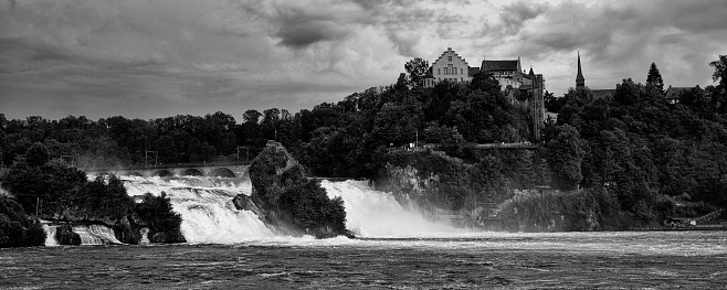 A black and white shot showing a dramatic sky with the powerful Rhine Falls in Switzerland.