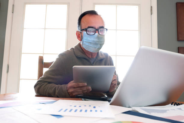 istock Hispanic Businessman Working From Home On Computer Wears Protective Face Mask 1262061960