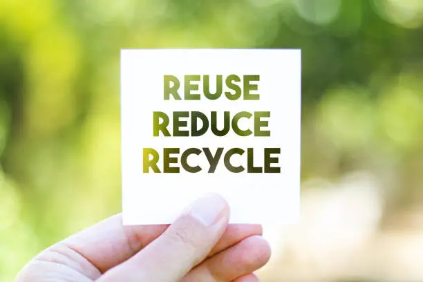 Holding the paper with REUSE REDUCE RECYCLE message in front of a beautiful blur nature background. Sustainability and environmental concept. Horizontal composition with copy space.