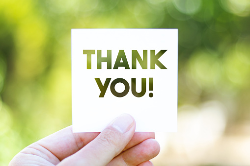 Holding the paper with Thank You message in front of a beautiful blur nature background. Sustainability and environmental concept. Horizontal composition with copy space.