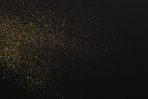 Gold glitter on black background. Design element. Golden grainy abstract texture on a black background. Holiday background
