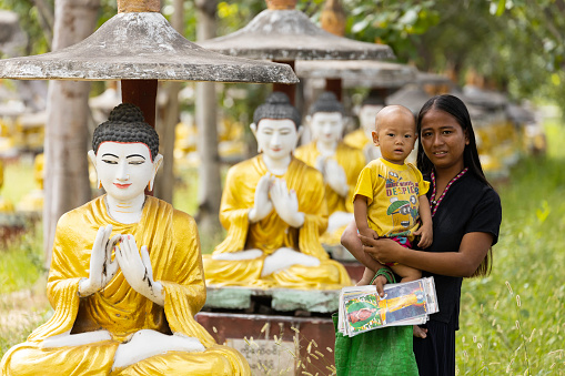 Sagaing/Myanmar-October 3rd 2019: A Burmese woman holds her child waiting to sell paintings to tourists in a temple.