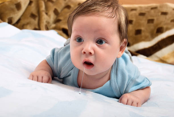 Cute little baby drool Cute little baby looks into the camera and drooling while lying on the bed. Creative concept photos spit stock pictures, royalty-free photos & images