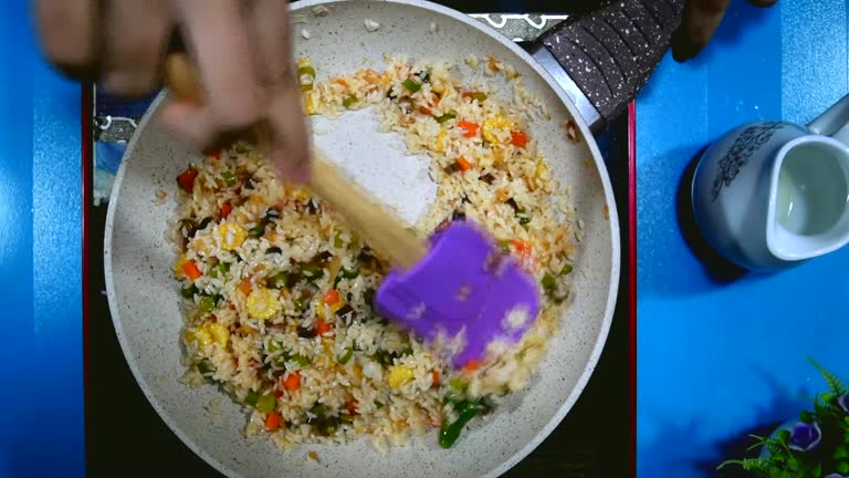 preparing a meal. Vegetables fried rice stirring in frying pan by spoon.