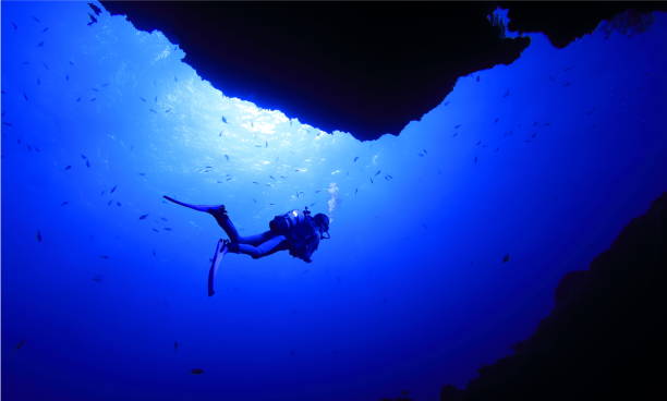 Diver swimming at the exit of the Queen's room A diver swimming at the exit of the Queen's room in a seabed cave at a diving spot in Miyakojima City, and sunlight pouring overhead. miyakojima island photos stock pictures, royalty-free photos & images