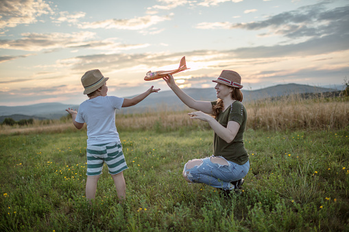 Boy and his mother on a field at sunset.Mum is holding a model of plane toy and shows her son how it flies.