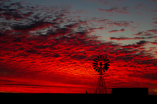 A silhouette of a windpomp in the Karoo with a brilliant red sunset behind. The background is full of red clouds.