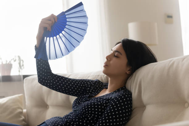 istock Unwell Asian girl feel overheated wave using hand fan 1262199829
