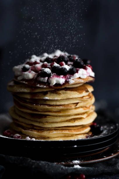 istock Stack of pancakes with sugar powder splashes on dark background table. 1262200200