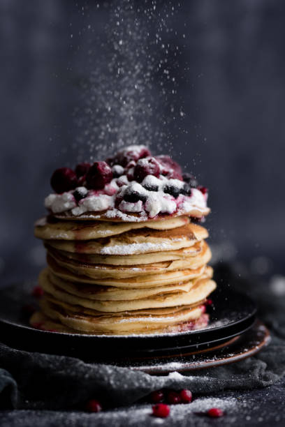 istock Stack of pancakes with sugar powder splashes on dark background table. 1262200789