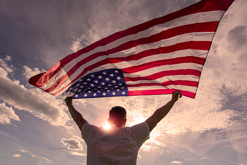 Man holding waving American USA flag in hands during warm sunny evening in USA, concept picture