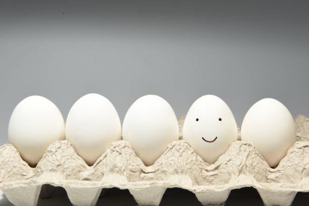 Smiley face on an egg shell A smiling face illustrated on an egg shell along with other white eggs in an egg tray. sabby stock pictures, royalty-free photos & images