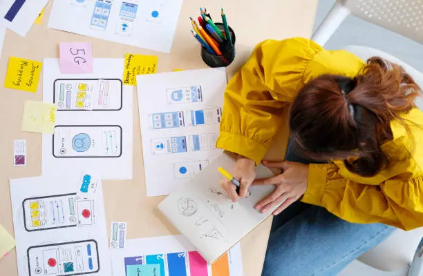 Photo of Website designer, Creative planning phone app development sketch template layout framework wireframe design, User experience concept, Overhead view of young woman UX designer thinking out web structure at home office