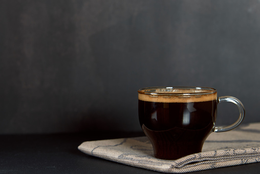 Taza de vidrio de café fresco caliente, cerveza de arábica, con espuma gruesa de espuma dorada sobre fondo oscuro. Espresso o americano, vertical, espacio de copia. photo