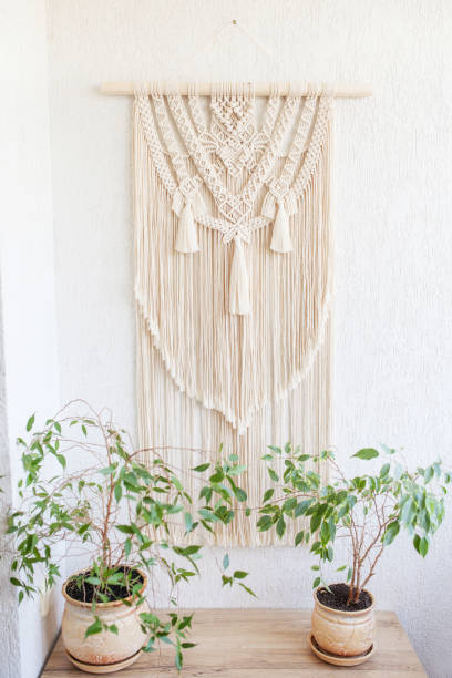 Handmade macrame. 100% cotton wall decoration with wooden stick hanging on a white wall.   Macrame braiding and cotton threads.  Female hobby.  ECO friendly modern knitting DIY natural decoration concept in the interior stock photo