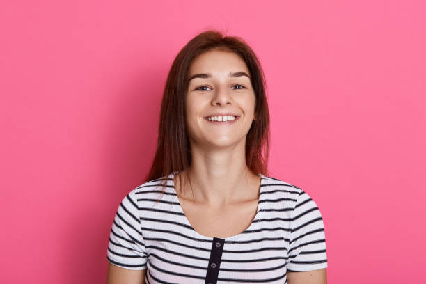 istock Young laughing woman against pink background looking directly at camera, posing isolated over pink background, wearing striped t shirt, girl expressing positive emotions. 1262236366