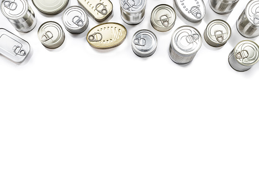 Top view of an assortment of canned food. All cans are closed and have different shapes and colors and are at the top of the image leaving a useful copy space at the lower side on a white background. Studio shot taken with Canon EOS 6D Mark II and Canon EF 24-105 mm f/4L