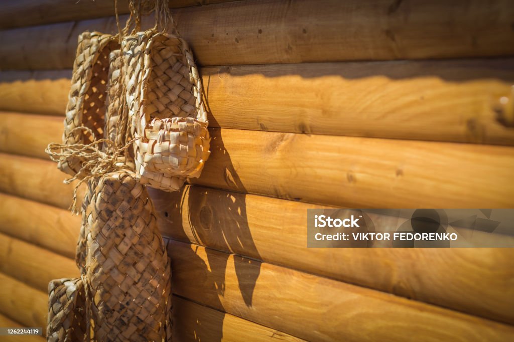 Birchen woven bast shoes hang on a log wall, selective focus Birchen woven bast shoes hang on a log wall, selective focus. Blank for the designer. Vintage accessories from country life. Ancient Stock Photo