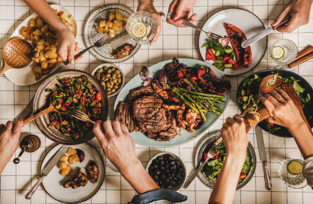 Flat-lay of summer barbeque family party woth various dishes Summer barbeque party. Flat-lay of table with grilled meat, vegetables, salads, roasted potato and peoples hands over white tablecloth, top view. Family gathering, feasting, comfort food concept eating asparagus stock pictures, royalty-free photos & images