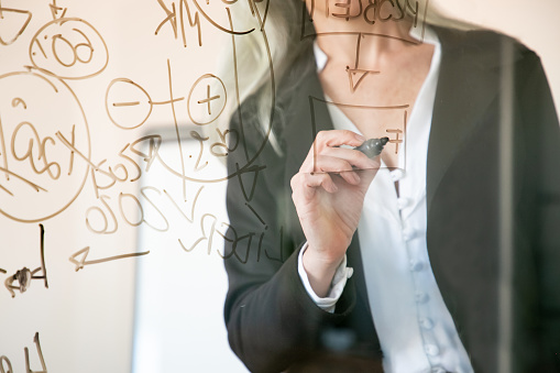 Unrecognizable grey-haired businesswoman writing on glass board. Hand holding black marker and making notes for project. Strategy, business and management concept