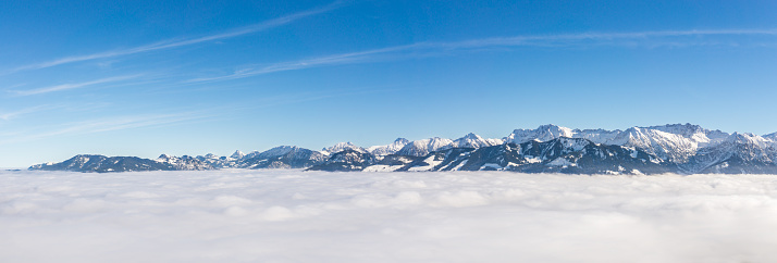 Awesome panoramic view of snow mountain range stick out of inversion fog layer. Great panorama with sunny blue sky above the clouds. Ofterschwanger Horn, Alps, Allgäu, Bavaria, Germany.