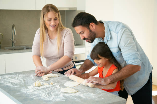 istock Positive mom and dad teaching daughter to roll dough 1262270473