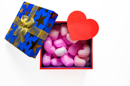 Gift or present box with filler with golden ribbon and paper heart on white background top view.
