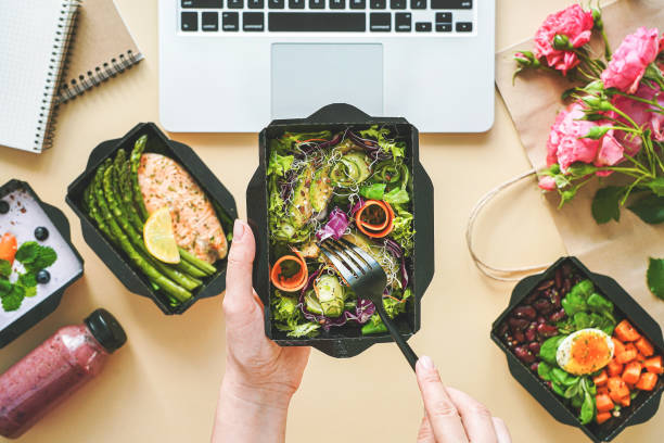 kobiece ręce trzymają pudełko na dostawę jedzenia z obiadem w pracy z domowego biura. business woman worker eats sałatka zabrać żywienia codziennie zdrowe menu diety odchudzania posiłek w miejscu pracy płaskie lay widok z góry. - lunch business office business lunch zdjęcia i obrazy z banku zdjęć